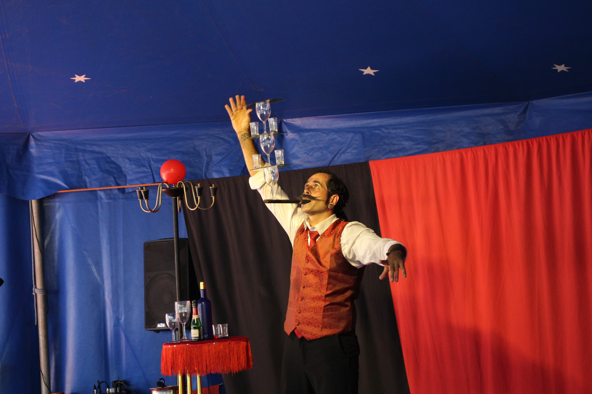 Artista a equilibrar copos numa tenda azul e vermelha