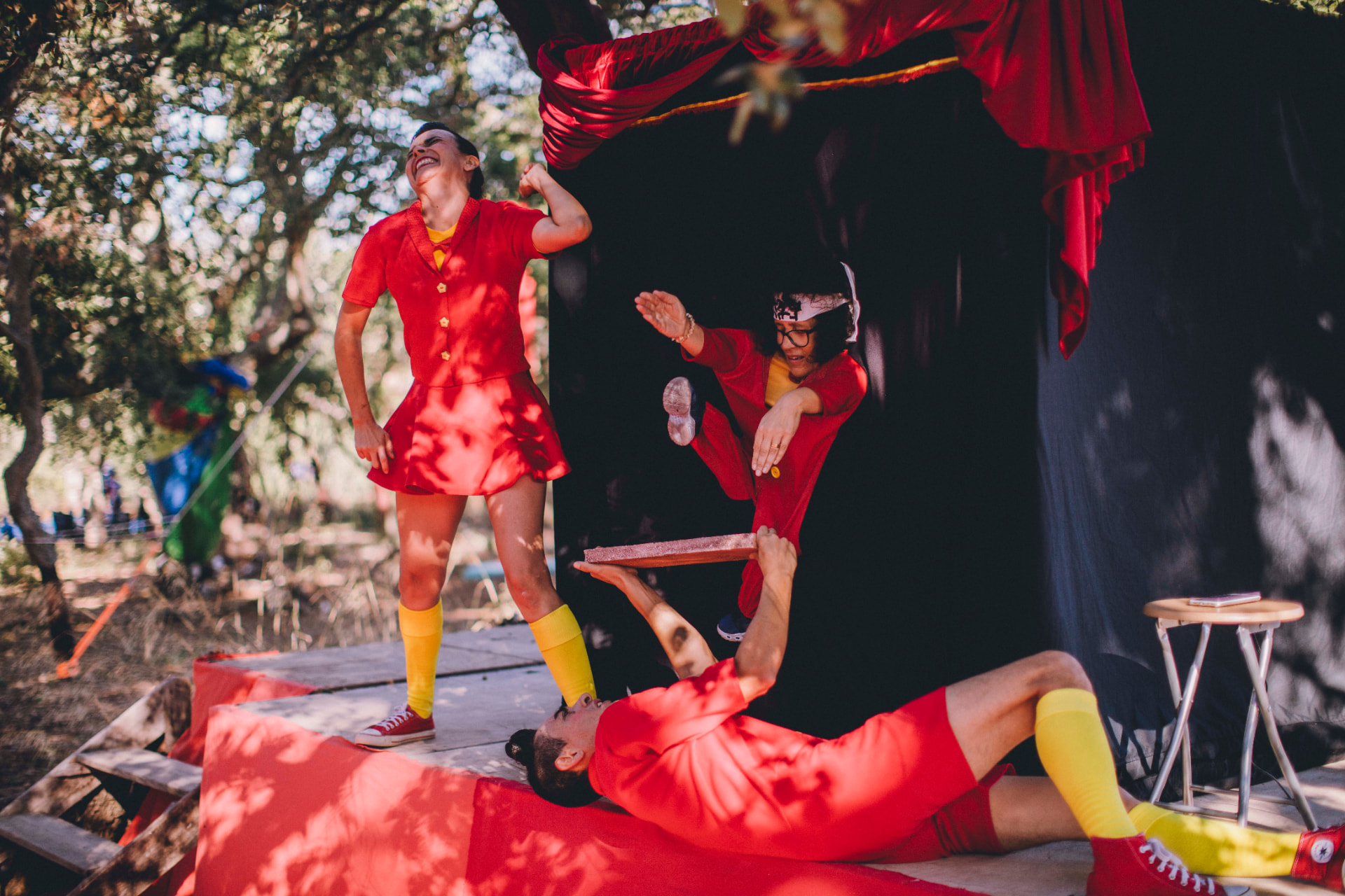 Trio de artistas vestidos de vermelho em espetáculo entre árvores