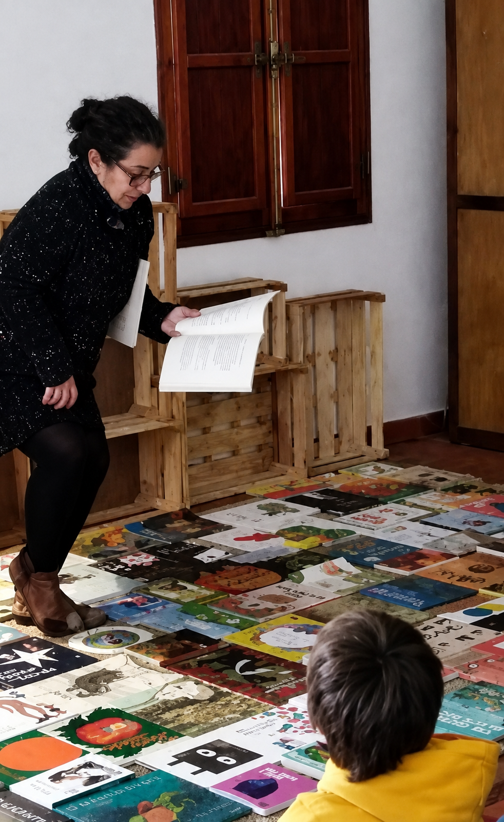 Manuela Pedroso com livros infantis espalhados no chão, a mostrar um livro aberto