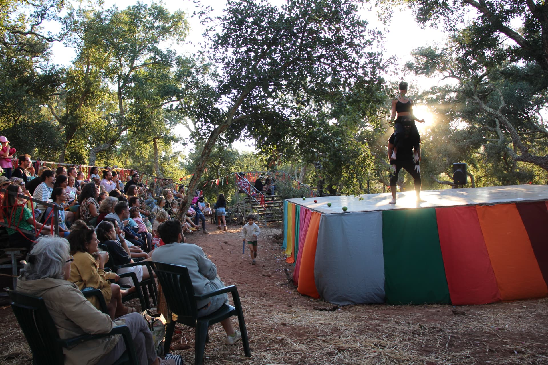 Público a assistir a espetáculo num palco colorido ao pôr do sol