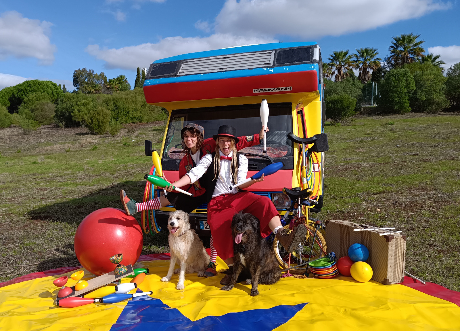 Artistas de circo em frente a uma caravana colorida com objetos de malabarismo